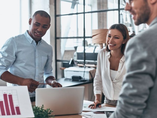 Team working together. Group of young modern people in smart casual wear discussing business while standing in the creative office